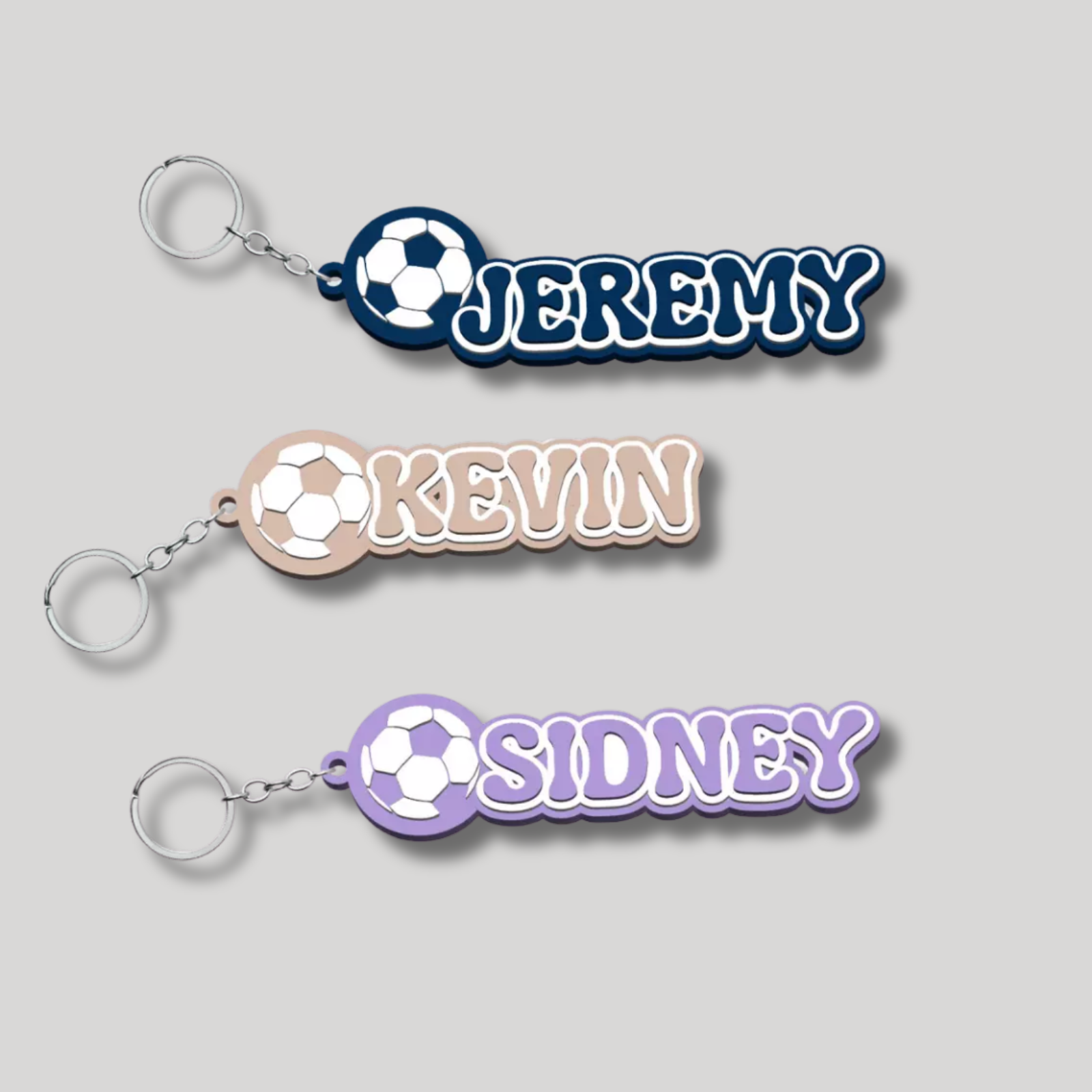 Group of three personalised retro football keyrings in navy ('Jeremy'), beige ('Kevin'), and purple ('Sidney').