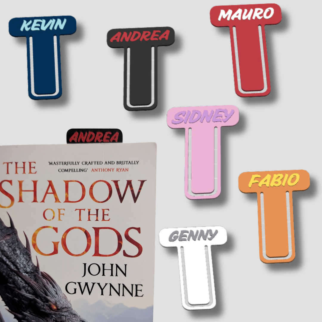 Assortment of seven personalised initial bookmarks in various colours, including Kevin, Andrea, Mauro, and Sidney, displayed around a book.