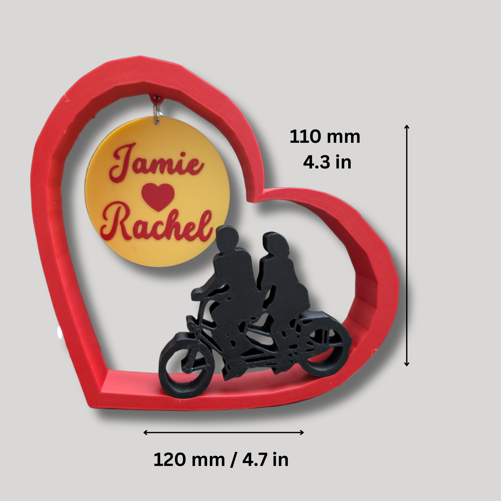 Decorative item with names on a yellow circle, surrounded by a red heart frame with silhouettes of two people on a motorcycle.