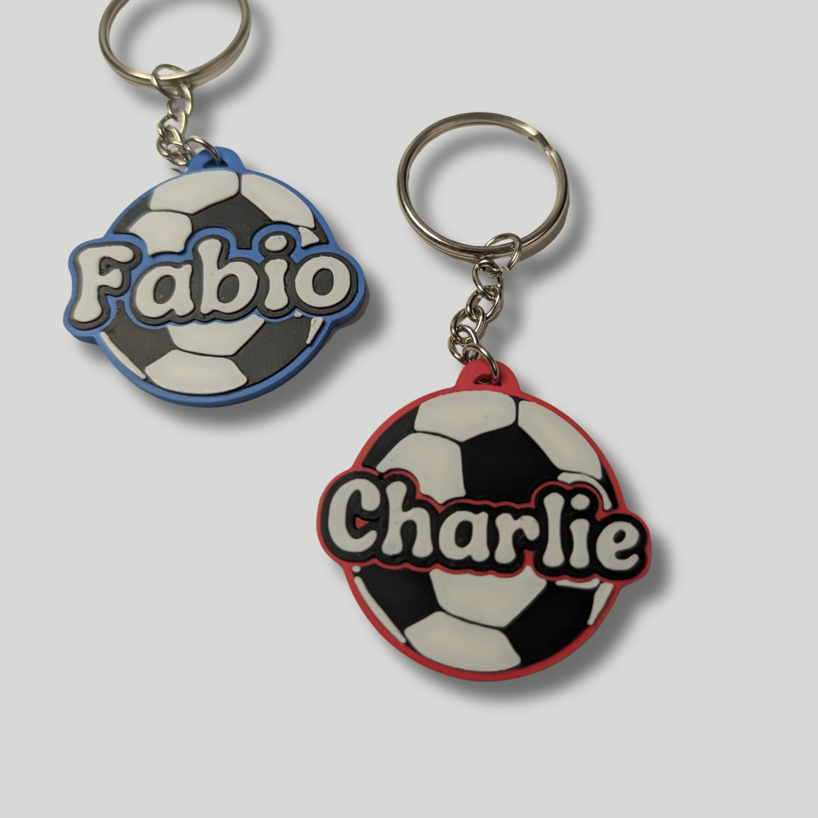 Two personalised football keyrings with custom names 'Fabio' (blue base) and 'Charlie' (red base).