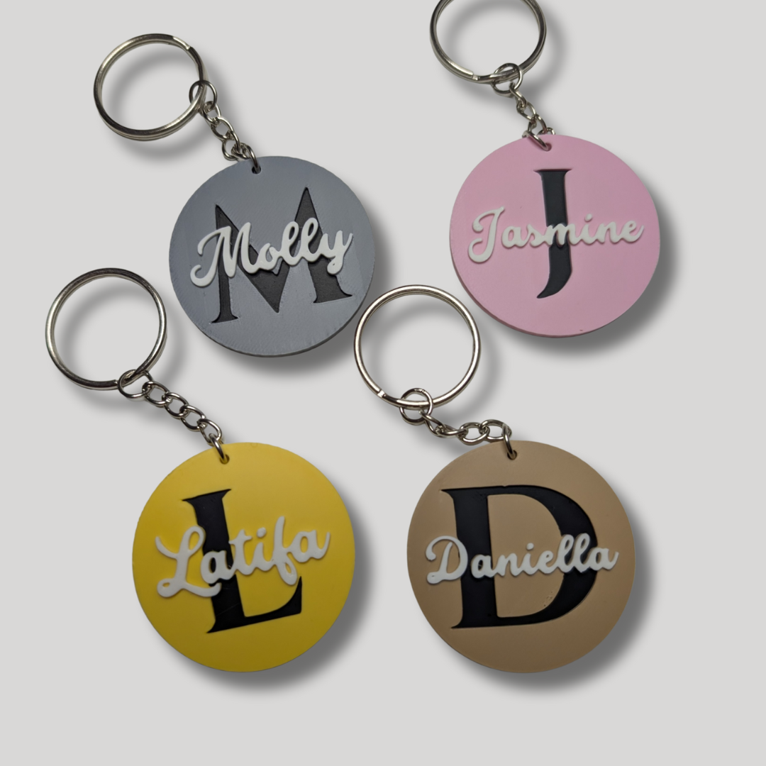 Four keychains with personalized names on circular tags against a light gray background