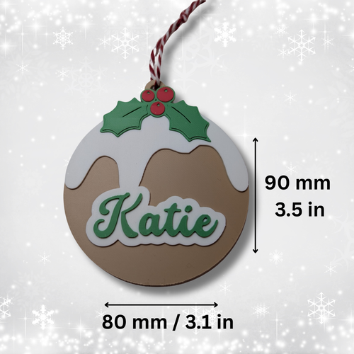Christmas pudding-shaped ornament with 'Katie' text, holly leaves, and berries on a white background.