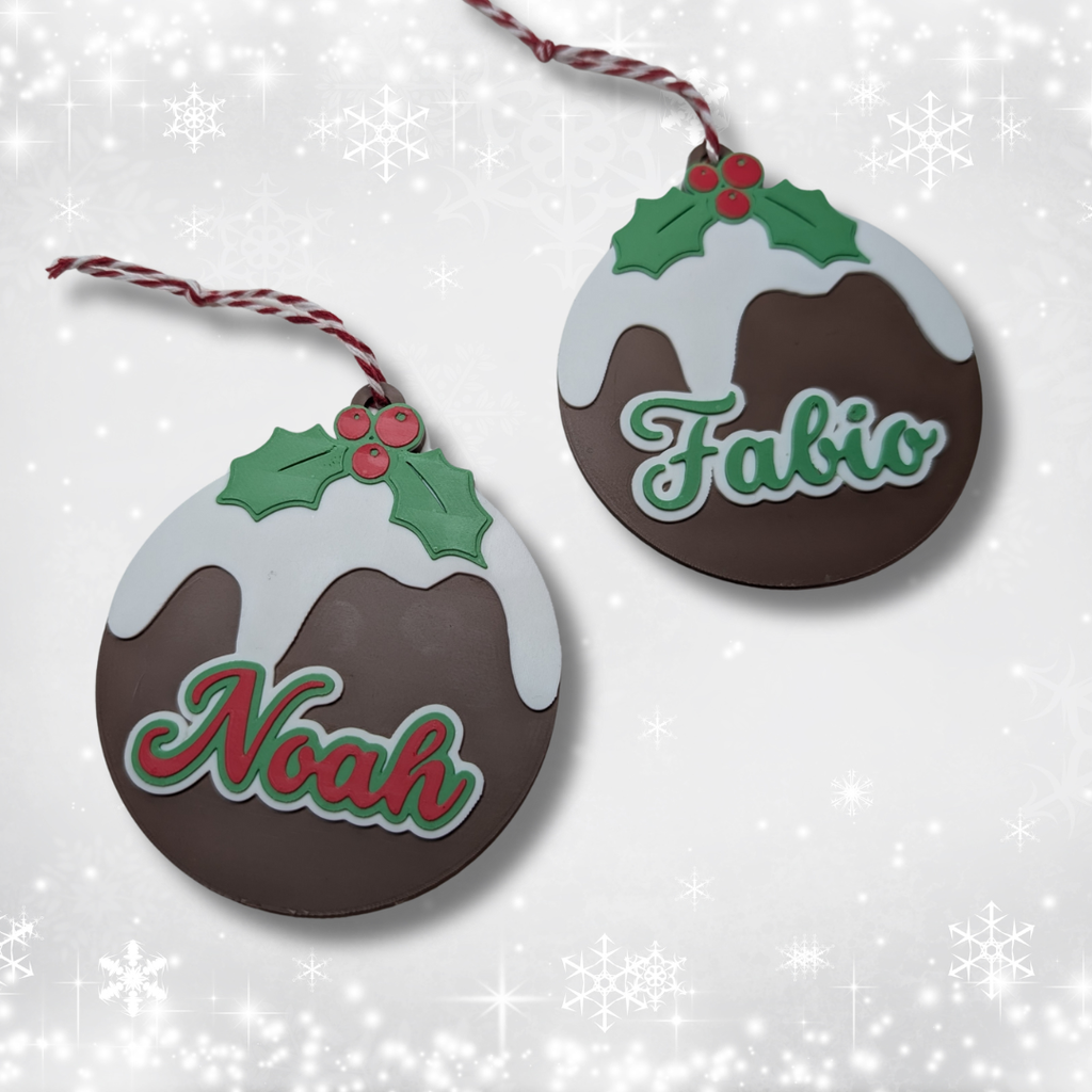 Two Christmas pudding-shaped ornaments with names 'Noah' and 'Fabio' on a snowy background.