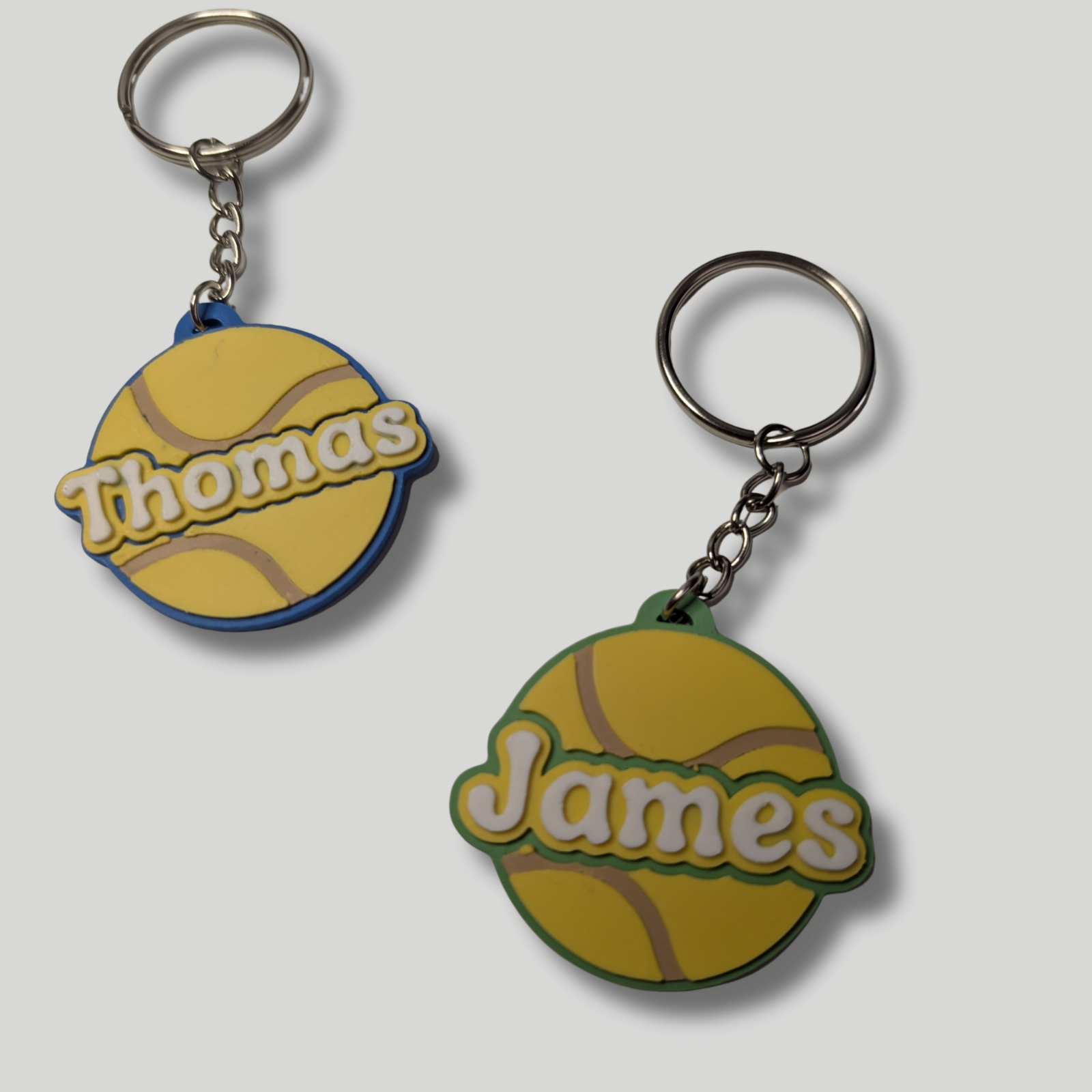 Two keychains shaped like tennis balls with 'Thomas' and 'James' engraved on a white background.
