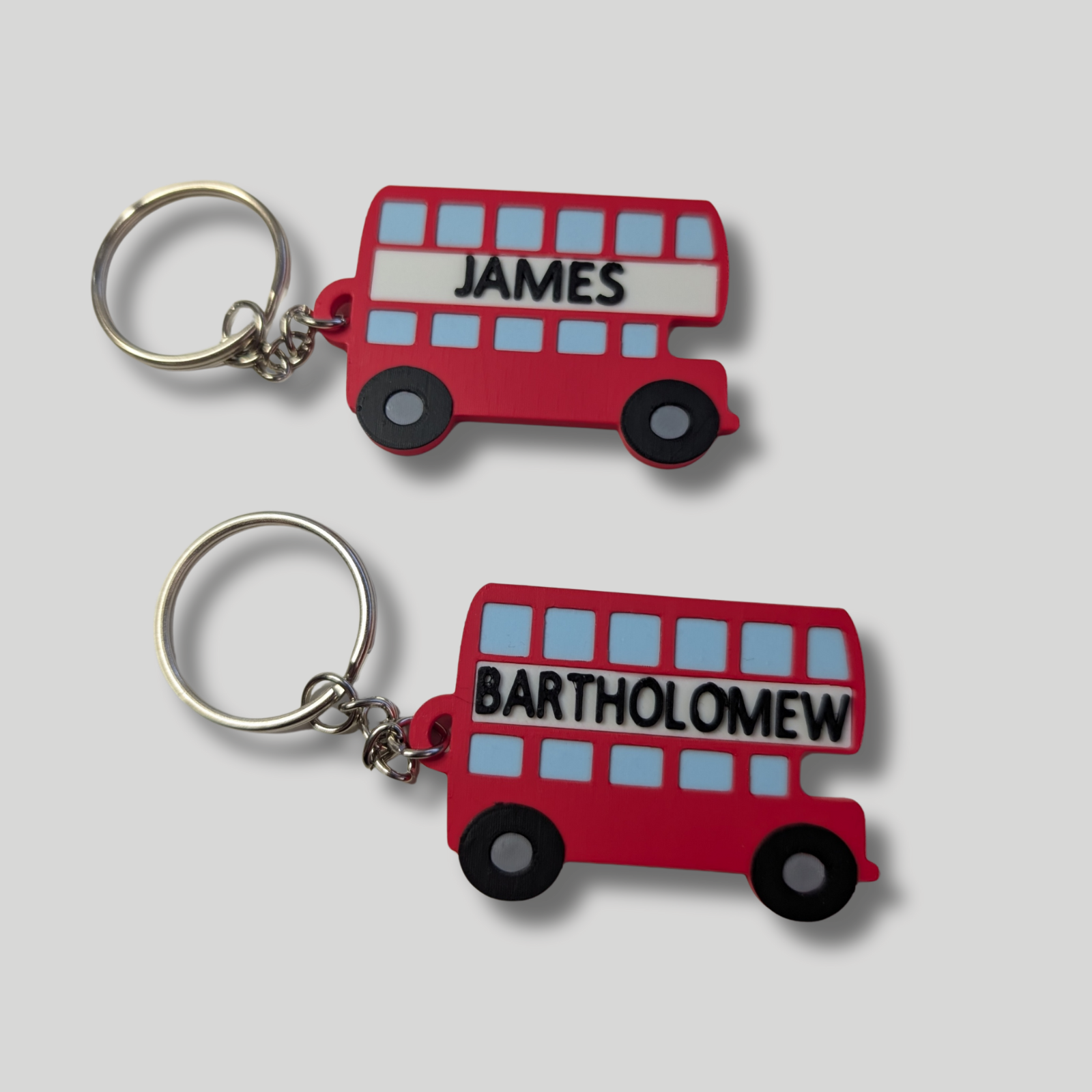 Two red bus-shaped keychains with names 'James' and 'Bartholomew' on a light gray background.
